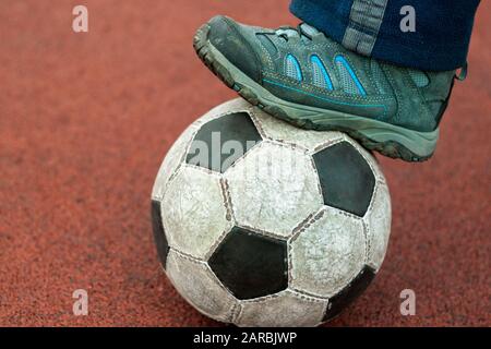 Pied humain dans une sneaker sale sur un vieux ballon de football. Banque D'Images