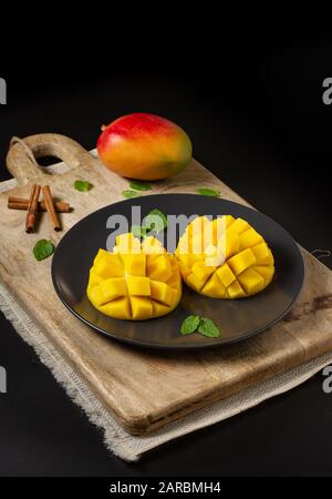 Coupe de mangue en deux et coudée sur une planche en bois, une branche entière de mangue et de cannelle, fond noir avec espace pour la copie Banque D'Images