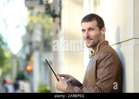 Homme adulte satisfait portant un casque tenant une tablette et vous regardant dans la rue Banque D'Images