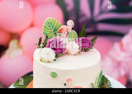 Gâteau rose avec flamingos pour les vacances. Gâteau avec une variété de décorations, feuilles de palmiers et fleurs fraîches. Banque D'Images