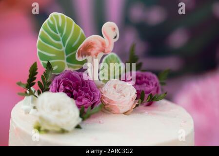 Gâteau rose avec flamingos pour les vacances. Gâteau avec une variété de décorations, feuilles de palmiers et fleurs fraîches. Banque D'Images