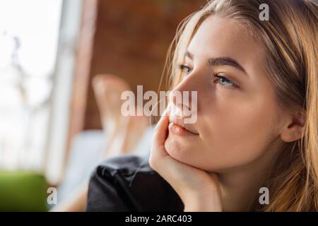 Journée de beauté pour vous-même. Femme portant une robe de soie faisant sa routine quotidienne de soin de la peau à la maison. Couché sur un canapé, regardant sur le côté, a l'air rêvant. Concept de beauté, auto-soins, cosmétiques, jeunes. Gros plan. Banque D'Images