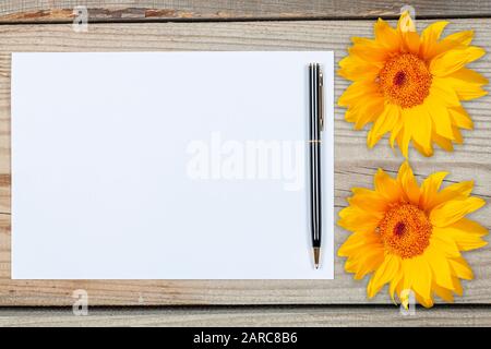 Une feuille de papier blanc entourée de tournesols sur un fond en bois. Banque D'Images