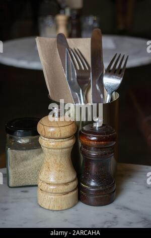 Grenaille verticale des fourches et des couteaux dans un récipient métallique avec sel et poivre sur une table Banque D'Images