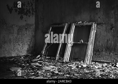 Prise de vue en niveaux de gris des cadres de fenêtre placés sur un sol désordonné dans une vieille maison Banque D'Images