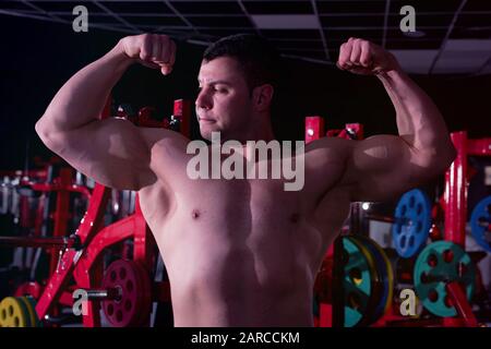 Modèle de forme physique homme posant dans la salle de gym. Beau homme avec de grands muscles, posant à l'appareil photo dans la salle de gym. Banque D'Images