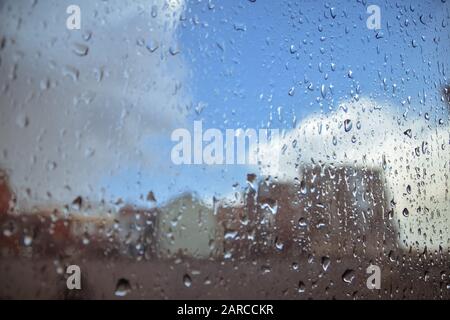 Gros plan d'un verre recouvert de gouttes de pluie avec des bâtiments en arrière-plan Banque D'Images