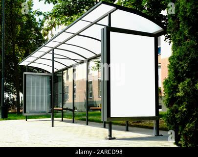 abri de bus structure de verre le long du trottoir de rue. pelouse verte et arbres luxuriants. scène d'été. panneaux publicitaires blancs. espace publicitaire. concept de marketing Banque D'Images