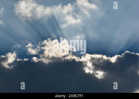 Rayons de soleil passant par les nuages sombres avec fond bleu ciel Banque D'Images