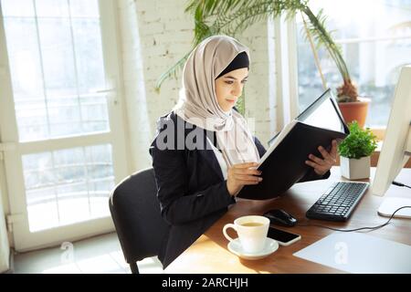 Examen des documents. Portrait d'une belle femme d'affaires arabe portant du hijab tout en travaillant dans un espace ouvert ou au bureau. Concept d'occupation, liberté dans le domaine des affaires, succès, solution moderne. Banque D'Images