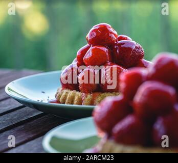 Deux tartes de fraises végétaliennes fraîches, servies sur des plaques vertes à une table en bois sur le balcon - vue latérale, carré, fond flou Banque D'Images