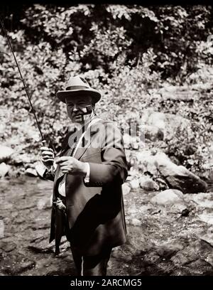 Le président américain Herbert Hoover - portant une cravate de costume et une fédora - pêche à la mouche dans un petit ruisseau en 1936. Banque D'Images