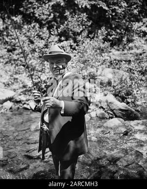 Le président américain Herbert Hoover - portant une cravate de costume et une fédora - pêche à la mouche dans un petit ruisseau en 1936. Banque D'Images