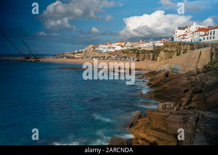 Large vue sur la ville d'Ericeira depuis la plage de sable avec le ciel spectaculaire et les maisons à flanc de falaise Banque D'Images