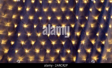 Guirlande festive avec de nombreuses lumières jaunes s'illuminent dans l'obscurité sur le fond. Décoration colorée et magique pour les vacances Banque D'Images