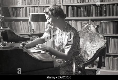 Années 1950, historique, une élégante dame dans son livre étude doublée assis à son bureau d'écriture antique, écrivant une lettre Londres, Angleterre, Royaume-Uni. Banque D'Images