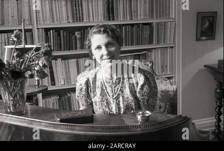 Années 1950, historique, une élégante dame dans son livre étude doublée assis à son ancien bureau d'écriture, Londres, Angleterre, Royaume-Uni. Banque D'Images