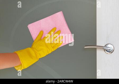 Concept de société de nettoyage commerciale. Le gant de protection en caoutchouc avec un chiffon en microfibre rose est une porte en verre essuyée. Banque D'Images