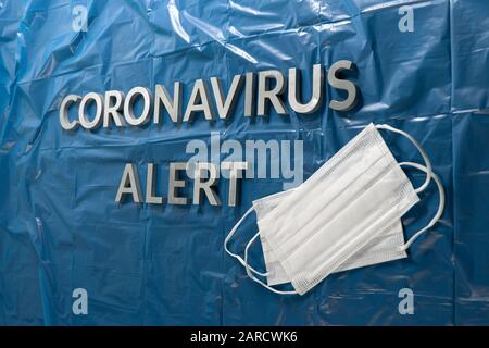 les mots coronavirus alert ont été mis en place avec des lettres argentées sur du bleu froissé revêtement en plastique - vue en perspective avec masques faciaux Banque D'Images