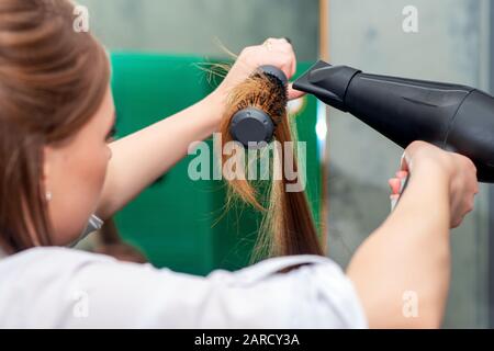 Coiffeur séchage cheveux longs brun avec sèche-cheveux et brosse ronde, gros plan. Banque D'Images