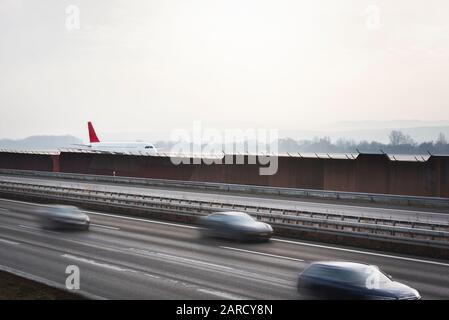 Avion blanc sur la piste et voitures rapides sur l'autoroute, près de l'aéroport de Stuttgart, Allemagne. Concept de transport des personnes. Déplacements rapides. Banque D'Images