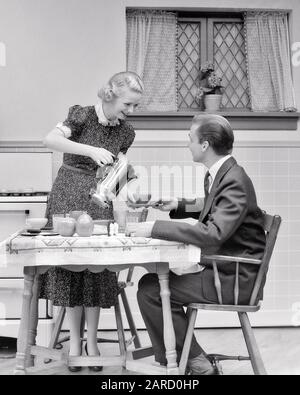 COUPLE DES ANNÉES 1930 DANS UN HOMME DE CUISINE ASSIS À UNE TABLE QUI LUI VERSE UNE TASSE DE CAFÉ - D3206 HAR001 HARS 1 STYLE DE COMMUNICATION BLONDE JEUNE ADULTE FORTE JOIE DE VIVRE SATISFACTION FEMMES MARIÉES STUDIO SHOT CONJOINT MARI MARI MAISON VIE ASSIS COPIE ESPACE AMITIÉ DEMI-LONGUEUR FEMMES SOINS HOMMES B&W MATIN PARTENAIRE FAMILLE COSTUME ET CRAVATE BONHEUR FEMMES AU FOYER SOURIRES SOUPERS JOYEUSES CAFÉINE ÉLÉGANT ATTACHEMENT PERSONNEL AFFECTION COOPÉRATION DÎNER ÉMOTION LUI AGITÉ ÉPOUSES JEUNE HOMME ADULTE JEUNE FEMME ADULTE NOIR ET BLANC CAUCASIEN HAR001 À L'ANCIENNE Banque D'Images