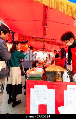 Regardez les gens qui achètent des boîtes en plastique de nouilles dans un étalage de nourriture avec une ligne de cuisiniers servant et préparant la nourriture au festival de la cerisier, au Japon Banque D'Images