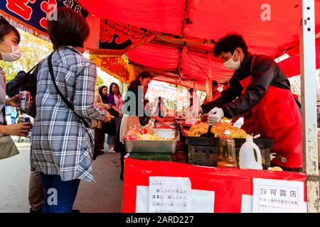 Regardez les gens qui achètent des boîtes en plastique de nouilles dans un étalage de nourriture avec une ligne de cuisiniers servant et préparant la nourriture au festival de la cerisier, au Japon Banque D'Images