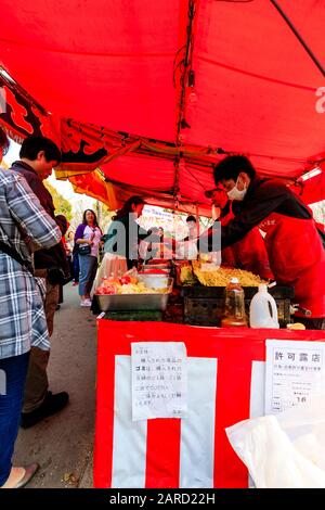 Regardez les gens qui achètent des boîtes en plastique de nouilles dans un étalage de nourriture avec une ligne de cuisiniers servant et préparant la nourriture au festival de la cerisier, au Japon Banque D'Images