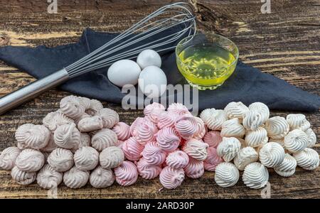 Gâteau meringue à tourbillon blanc, fouetté, gris et rose nommé Pavlova dans le processus de préparation. Tourbillons de beze blancs, gris et roses sur table en bois. Banque D'Images