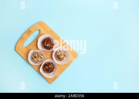 Diverses boulettes d'énergie maison faites de fruits secs, de noix et de graines à bord de bois sur fond bleu pastel Banque D'Images