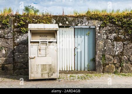 Vila Cha près d'Esposende, Portugal - 9 mai 2018: Conteneurs publics pour récupérer le jouet et les vêtements (Roupa Brincedos) devant un mur de pierre dans le c Banque D'Images