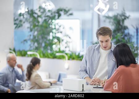 Taille vers le haut portrait de jeune homme parlant à un ami asiatique tout en se tenant au grand bureau, espace de copie Banque D'Images