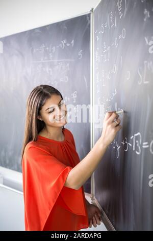 Jolie jeune étudiant écrit sur le tableau/blackboard pendant un cours de mathématiques. Banque D'Images