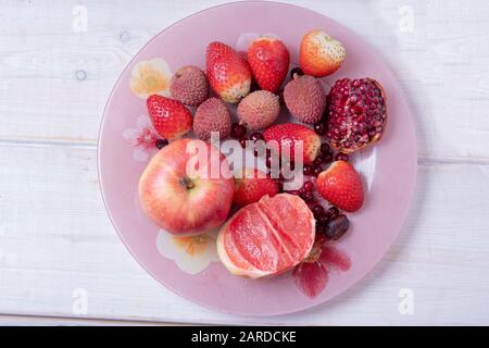 Fruits rouges et roses sur plaque rose sur surface en bois blanc ( aussi vibernum et lychee ) Banque D'Images