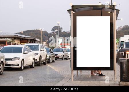 À l'arrêt de bus, le panneau publicitaire est blanc creux. Il y a des véhicules garés à gauche et à droite. Banque D'Images