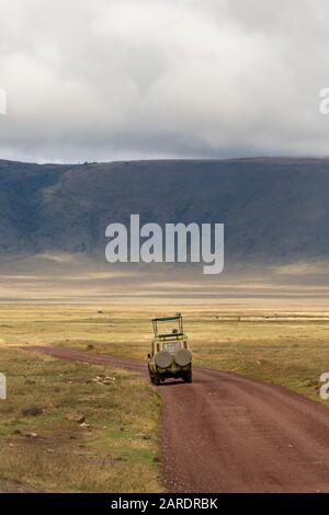 4 x 4 véhicule Safari conduisant sur la route de terre dans le cratère de Ngorongoro avec herbe verte et la jante de cratère en arrière-plan. Banque D'Images