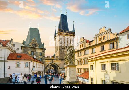 Les touristes marchent sur le pont Charles à travers la tour de Mala Strana et s'arche dans le quartier de la petite ville de Prague au coucher du soleil. Banque D'Images