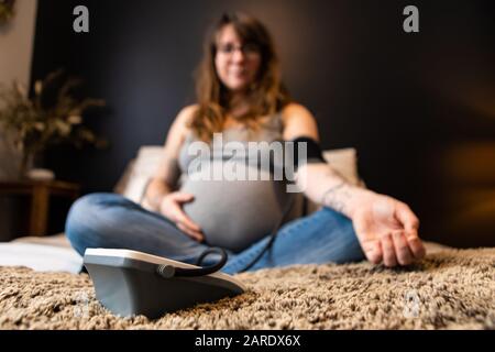 Une faible profondeur de champ avec une femme enceinte floue assise sur un lit, effectuer des contrôles de santé prénatale en préparation à la naissance à la maison. Copier l'espace sur les côtés Banque D'Images