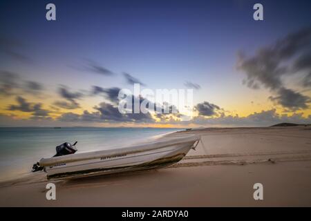 Petit dingy avec moteur extérieur sur la plage au coucher du soleil Banque D'Images