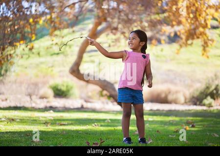 Une jeune fille qui s'amuse à jouer avec une branche dans un beau parc en automne. Banque D'Images