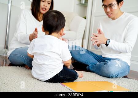 Famille asiatique heureuse de trois, jeune père et mère jouant à des jeux et se clamant les mains avec bébé garçon enfant à la maison, parents profitant de l'heure de famille Banque D'Images