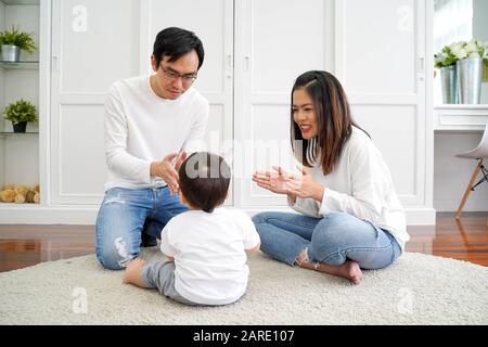 Famille asiatique heureuse de trois, jeune père et mère jouant à des jeux et se clamant les mains avec bébé garçon enfant à la maison, parents profitant de l'heure de famille Banque D'Images