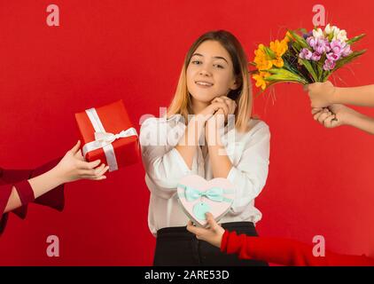 Tous les cadeaux et les fleurs. Célébration de la Saint-Valentin. Heureuse fille caucasienne mignonne isolée sur fond de studio rouge. Concept d'émotions humaines, expression faciale, amour, relations, vacances romantiques. Banque D'Images