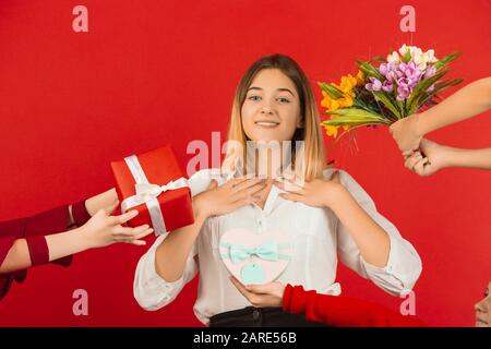 Tous les cadeaux et les fleurs. Célébration de la Saint-Valentin. Heureuse fille caucasienne mignonne isolée sur fond de studio rouge. Concept d'émotions humaines, expression faciale, amour, relations, vacances romantiques. Banque D'Images