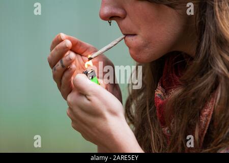 Gros plan de la photo de la femme caucasienne avec la main roulé joint de marijuana tenu dans ses lèvres tandis que ses doigts tatoués éclaient le cannabis jay. Banque D'Images