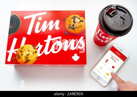 Calgary (Alberta). Canada 27 Janvier 2020. Une personne utilisant un iPhone plus en utilisant l'application Tim Hortons avec un café et une boîte de beignets sur fond blanc Banque D'Images
