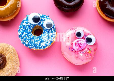 Un beignet bleu avec un beignet rose avec des visages drôles sur un fond rose se regardant l'un l'autre Banque D'Images