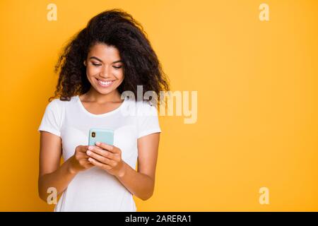 Photo d'une jolie jolie petite amie charmante et chaleureuse regardant dans un smartphone souriant et émignant, isolée à la recherche d'un nouveau Banque D'Images