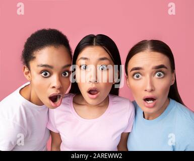 Trois Filles Surprise Regardant L'Appareil Photo Poser Sur Fond Rose Banque D'Images